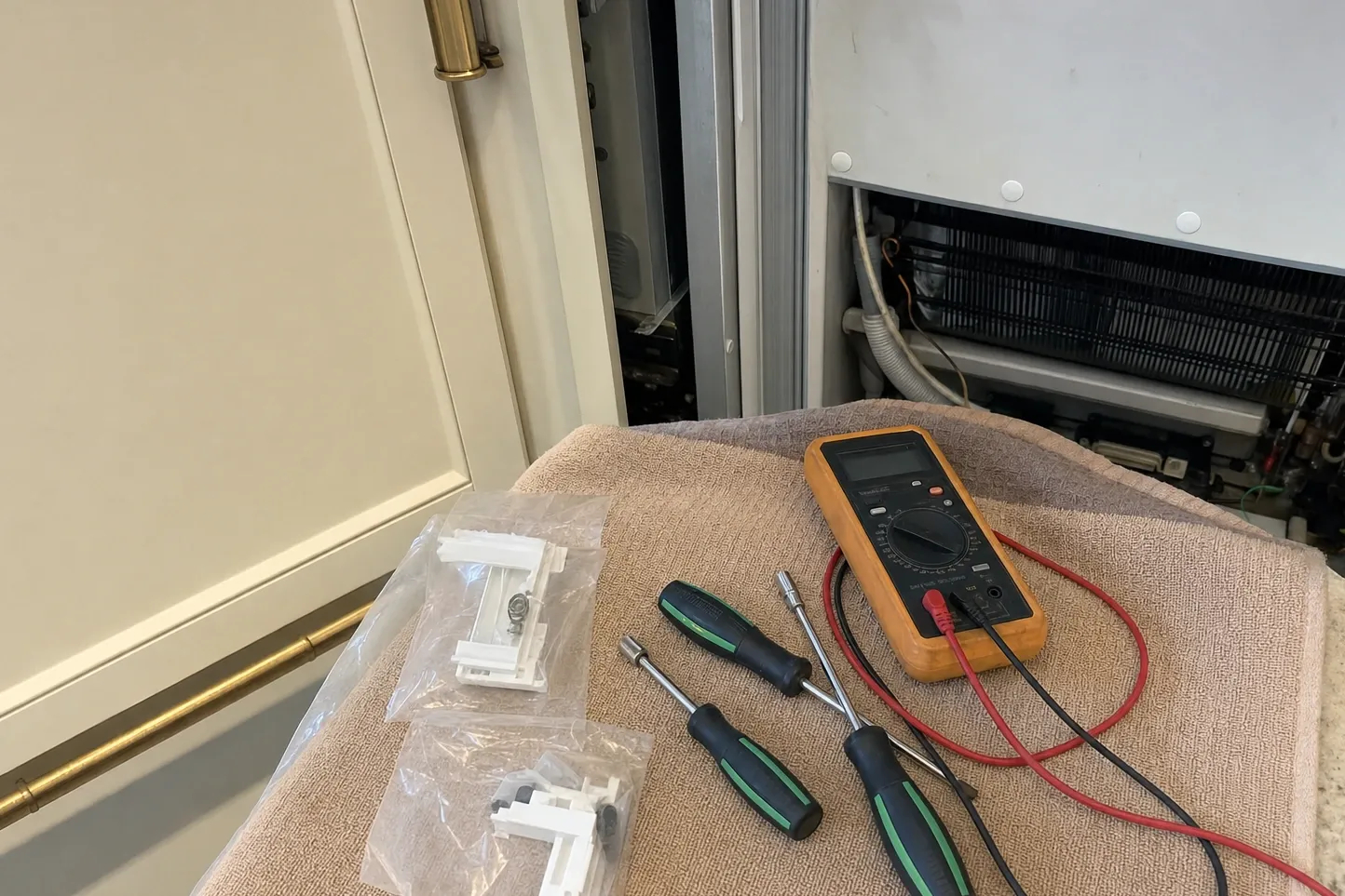 Orange multimeter with test leads, two screwdrivers and bagged replacement plastic parts laid out on a towel